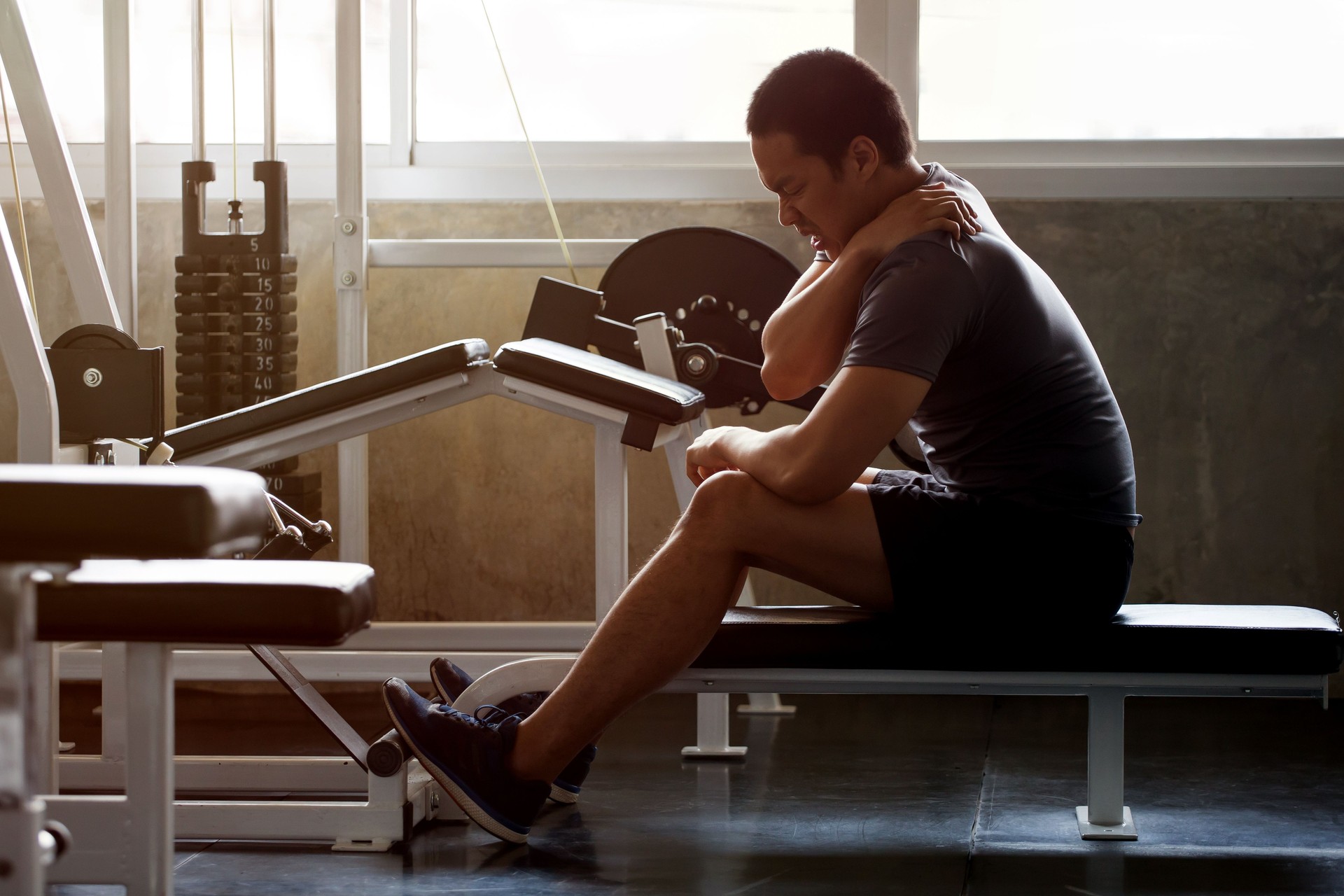 asian Muscular man suffering from shoulder injury while exercising at gym in morning light . workout , exercises , bodybuilder training , sport guy rubbing his back and neck pain .  backache